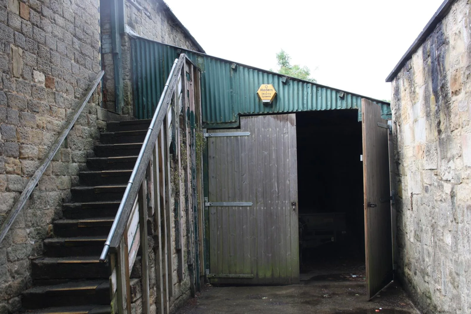 The lean-to, a green corrugated roof over timber doors beside the external stone steps